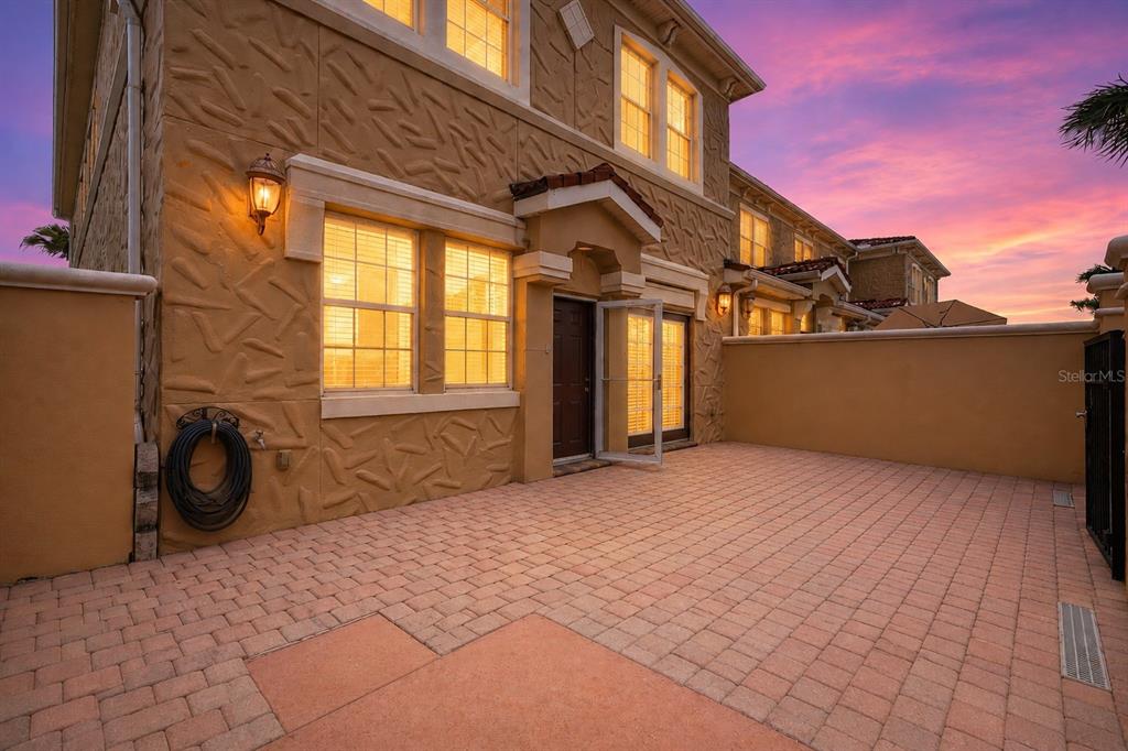 A paved patio area sits in front of a two-story stucco townhouse at sunset — 2828 BELLA VISTA DRIVE, DAVENPORT, FL