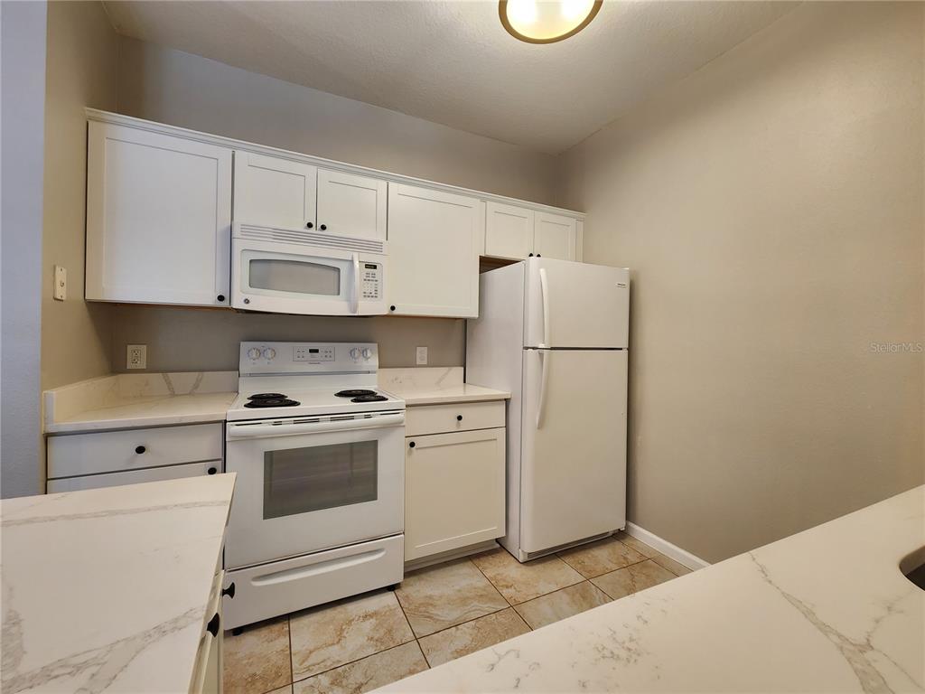 A kitchen features white cabinets, white appliances, and light-colored countertops with a tile floor — 4802 51ST STREET W UNIT 1421, BRADENTON, FL