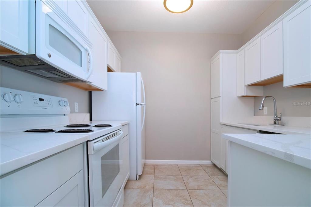 A kitchen features white cabinets, white appliances, light countertops, and beige tiled flooring — 4802 51ST STREET W UNIT 1421, BRADENTON, FL
