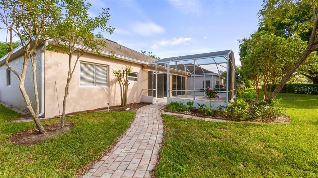 A paved walkway leads to the screened-in patio of a tan house with a lawn — 2241 KINGSMILL WAY, CLERMONT, FL
