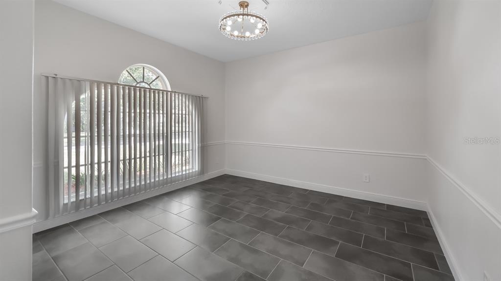 A dining room with gray tile flooring, white walls, a chandelier, and a large window — 2241 KINGSMILL WAY, CLERMONT, FL