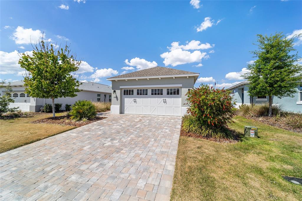 A single-story house exterior features a white two-car garage and a paved stone driveway — 10323 SW 98TH PLACE ROAD, OCALA, FL