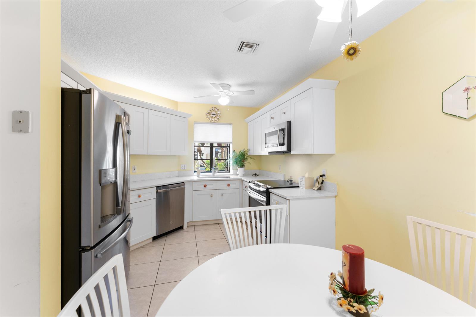 A kitchen with white cabinets, stainless steel appliances, and yellow walls features a dining area — 5226 Europa Drive # G, Boynton Beach FL 33437, BOYNTON BEACH, FL