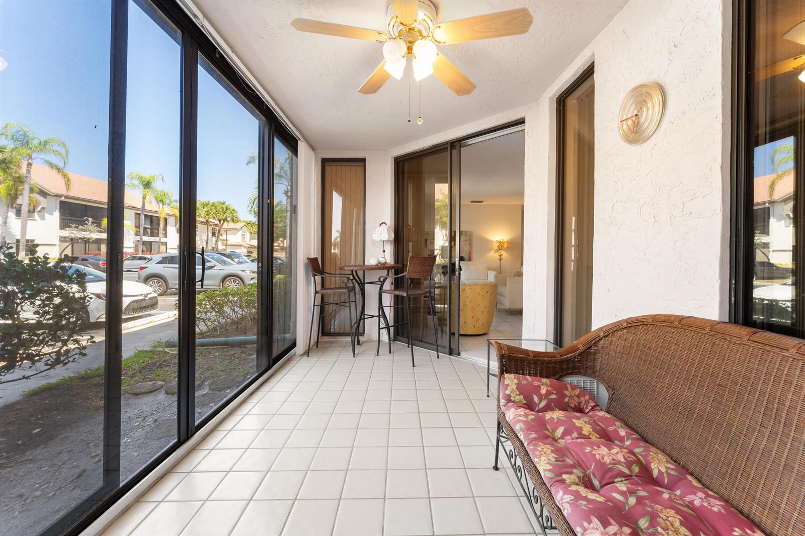 A sunroom features a wicker loveseat, a small bistro set, tile flooring, and sliding glass doors — 5226 Europa Drive # G, Boynton Beach FL 33437, BOYNTON BEACH, FL