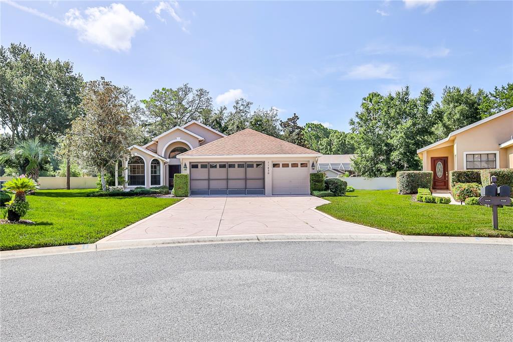 A single-story house with a three-car garage and a concrete driveway under a blue sky — 11430 KINGSTREE COURT, SPRING HILL, FL