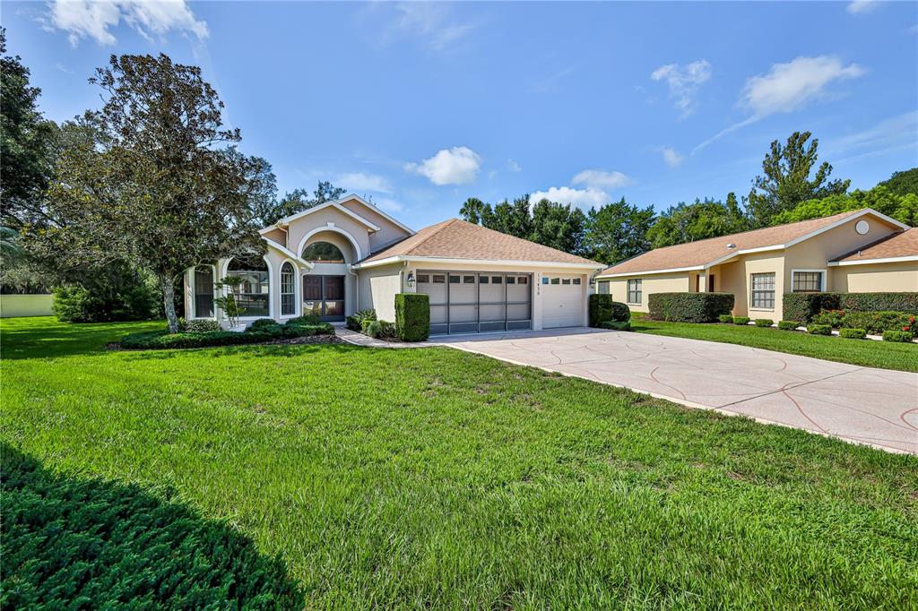 A single-story house with a beige stucco exterior, a two-car garage, and a large lawn — 11430 KINGSTREE COURT, SPRING HILL, FL
