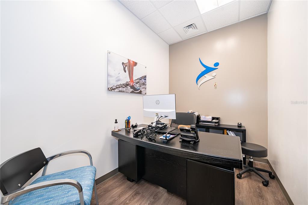 A small office features a black desk, a computer monitor, and a blue guest chair — 7560 RED BUG LAKE RD UNIT 2010, OVIEDO, FL