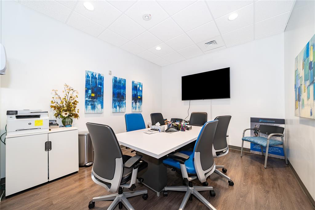 A conference room features a white table, six office chairs, a wall-mounted television, and artwork — 7560 RED BUG LAKE RD UNIT 2010, OVIEDO, FL
