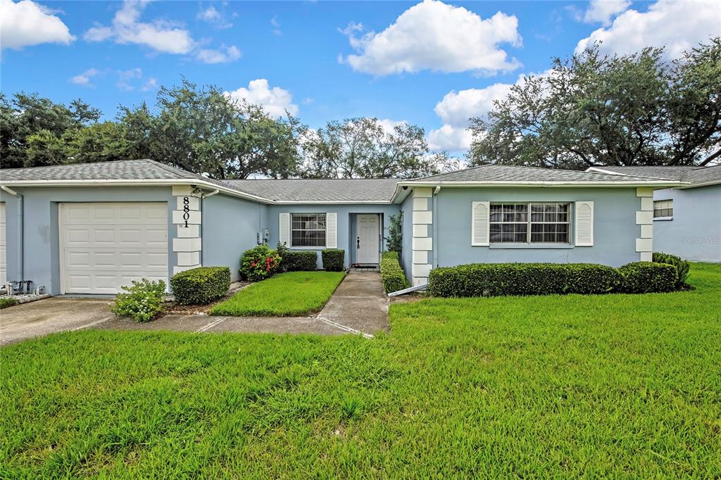 A single-story light blue house with a white garage door and a front lawn — 8801 MANOS CIRCLE UNIT 8801, NEW PORT RICHEY, FL