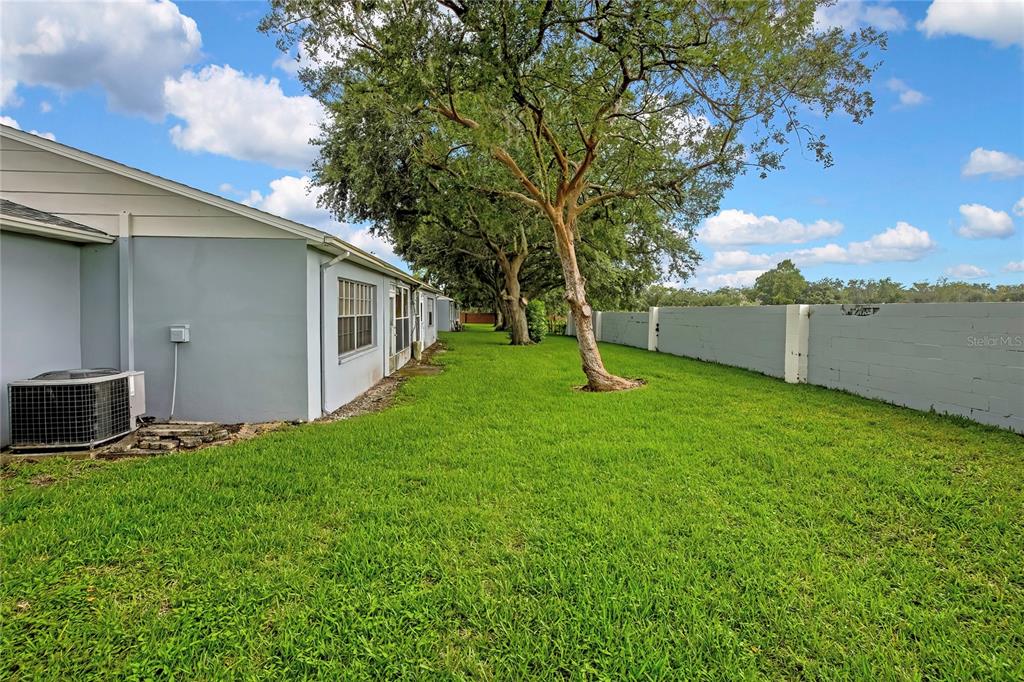 A side view of a house exterior with a lawn, trees, and a concrete wall — 8801 MANOS CIRCLE UNIT 8801, NEW PORT RICHEY, FL