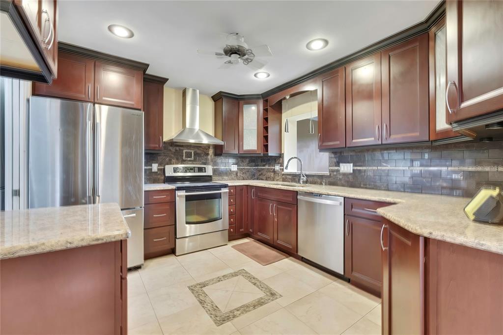 A kitchen features dark wood cabinets, stainless steel appliances, granite countertops, and a tiled floor — 8801 MANOS CIRCLE UNIT 8801, NEW PORT RICHEY, FL