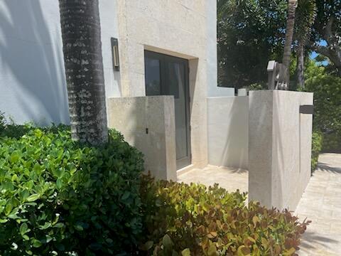 A stone-walled exterior entryway features a glass door, a palm tree, and lush green landscaping — 1955 NE 4th Street Unit 1, Deerfield Beach FL 33441, DEERFIELD BEACH, FL
