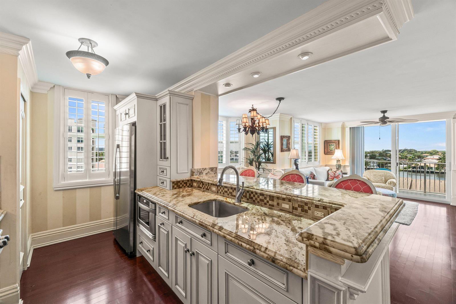 A kitchen with granite countertops and white cabinetry overlooks a living area with balcony views — 3594 S Ocean Boulevard # 801, Highland Beach FL 33487, HIGHLAND BEACH, FL