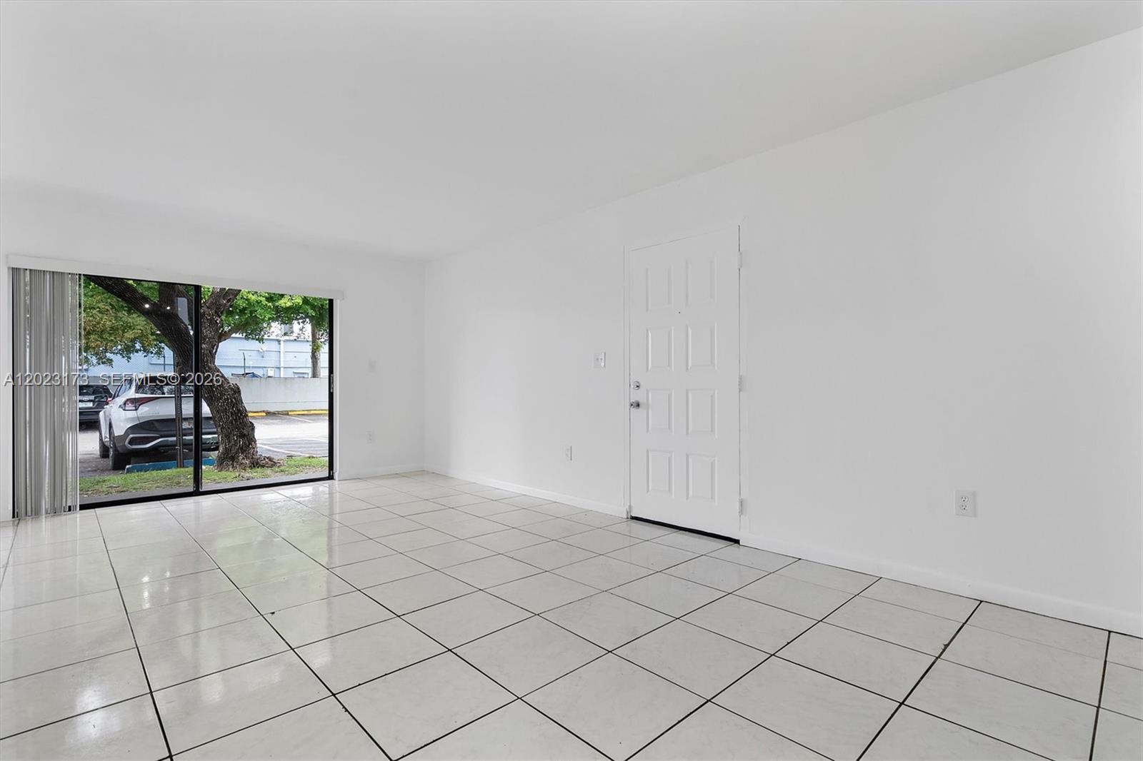 An empty room features white walls, white tile flooring, a sliding glass door, and an entrance — 7407 SW 152nd Ave # 103, Miami FL 33193, MIAMI, FL