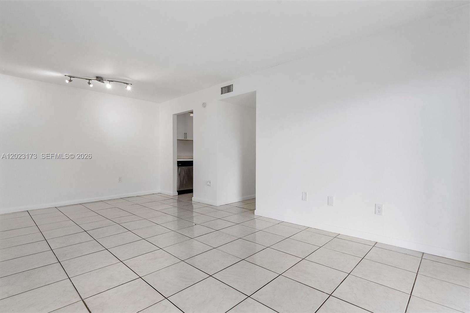 An empty room with white walls, tile flooring, and a doorway leading to a kitchen — 7407 SW 152nd Ave # 103, Miami FL 33193, MIAMI, FL
