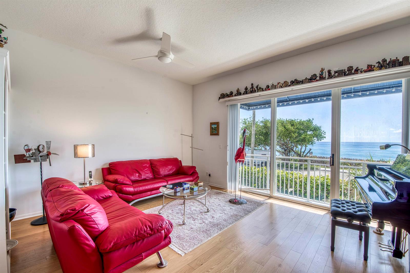 A living room with two red leather sofas, a piano, and sliding doors overlooking the ocean — 115 Ocean Key Way, Jupiter FL 33477, JUPITER, FL