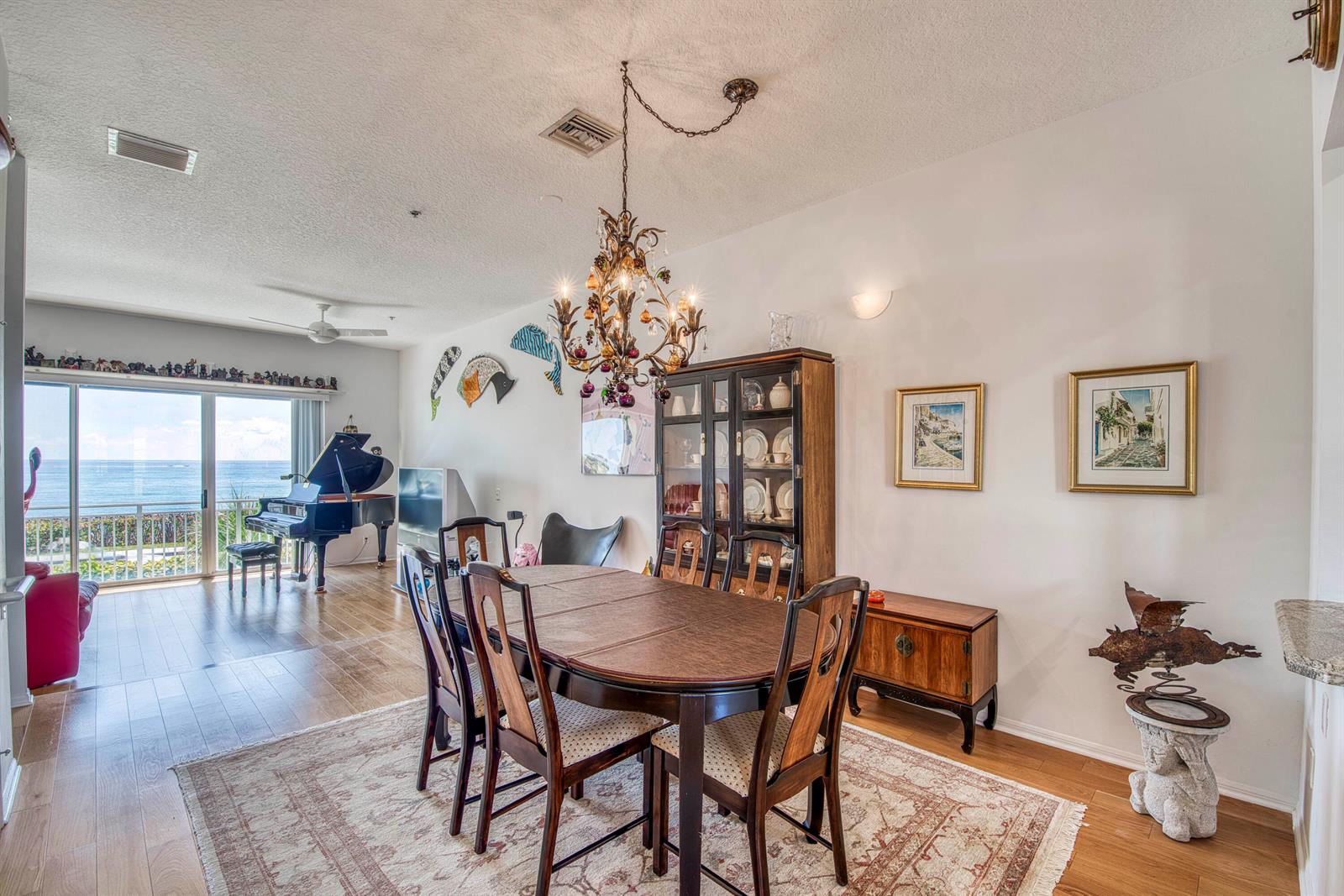 A dining room with a wooden table, chandelier, and a grand piano overlooking the ocean — 115 Ocean Key Way, Jupiter FL 33477, JUPITER, FL