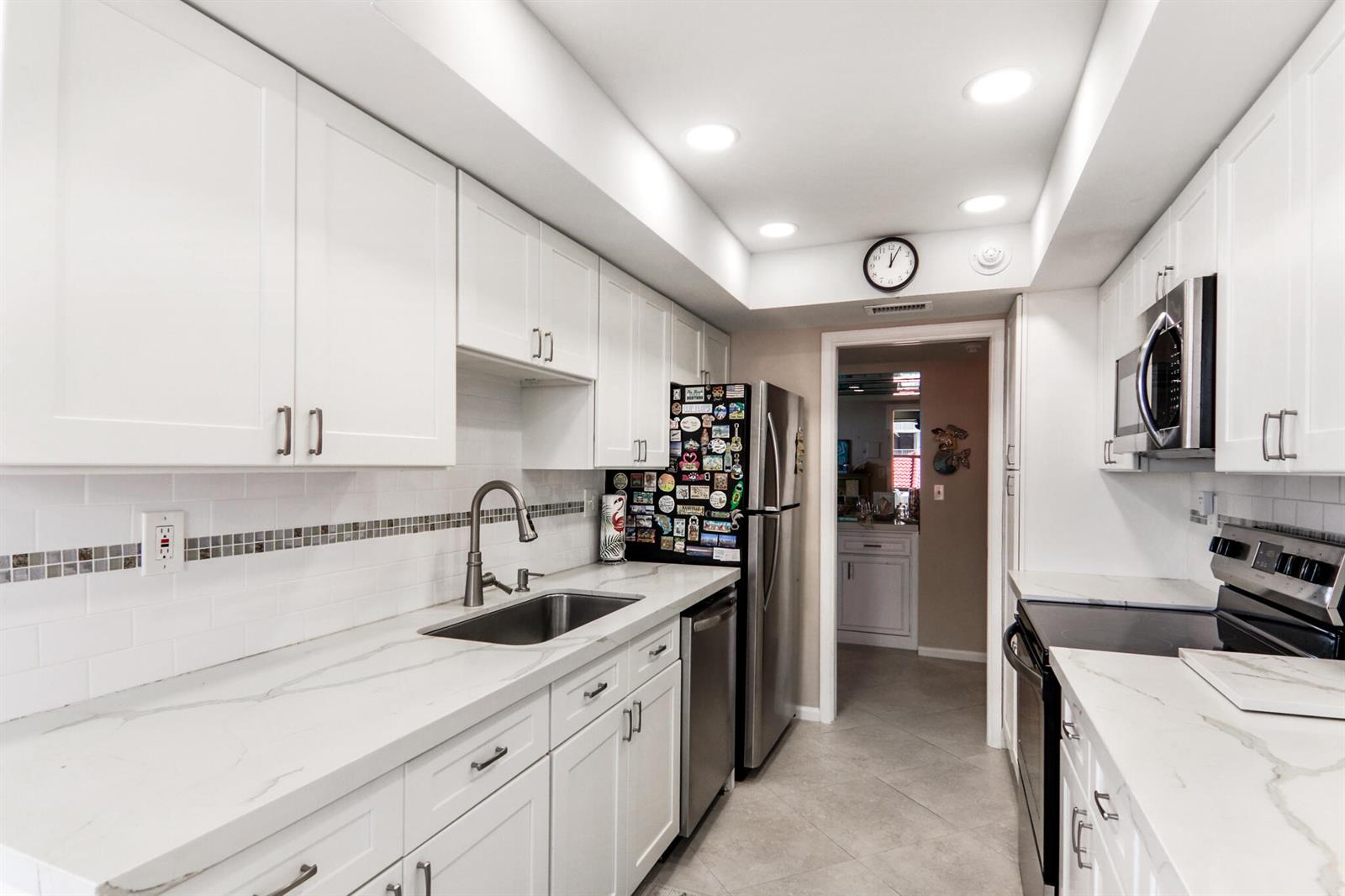 A galley kitchen features white cabinets, marble-look countertops, stainless steel appliances, and a tiled backsplash — 5480 N Ocean Drive, Singer Island FL 33404, SINGER ISLAND, FL
