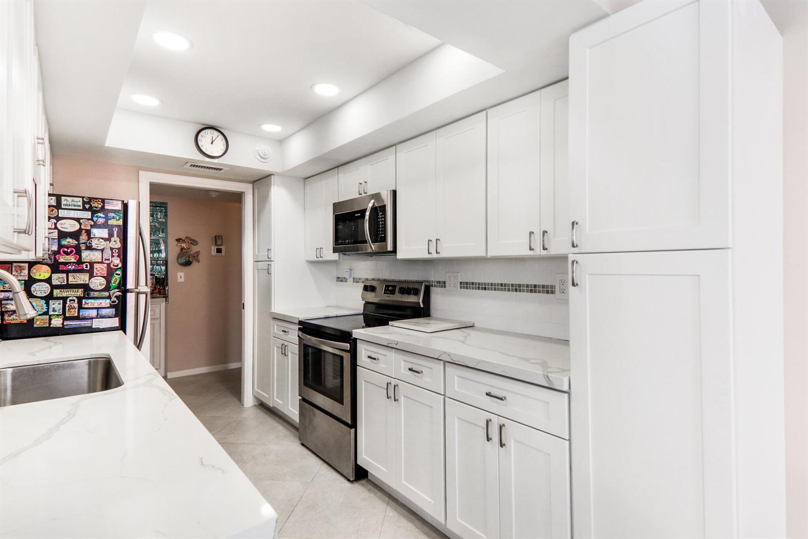 A kitchen features white cabinets, stainless steel appliances, and white marble-look countertops — 5480 N Ocean Drive, Singer Island FL 33404, SINGER ISLAND, FL