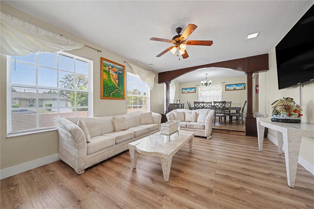 A living room with light wood floors, two white sofas, and an arched dining area — 6203 TEBBETTS DRIVE, ORLANDO, FL
