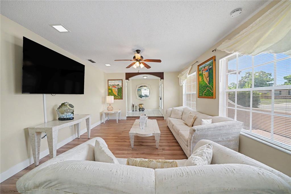 A living room features white sofas, wood-look flooring, a wall-mounted television, and large windows — 6203 TEBBETTS DRIVE, ORLANDO, FL