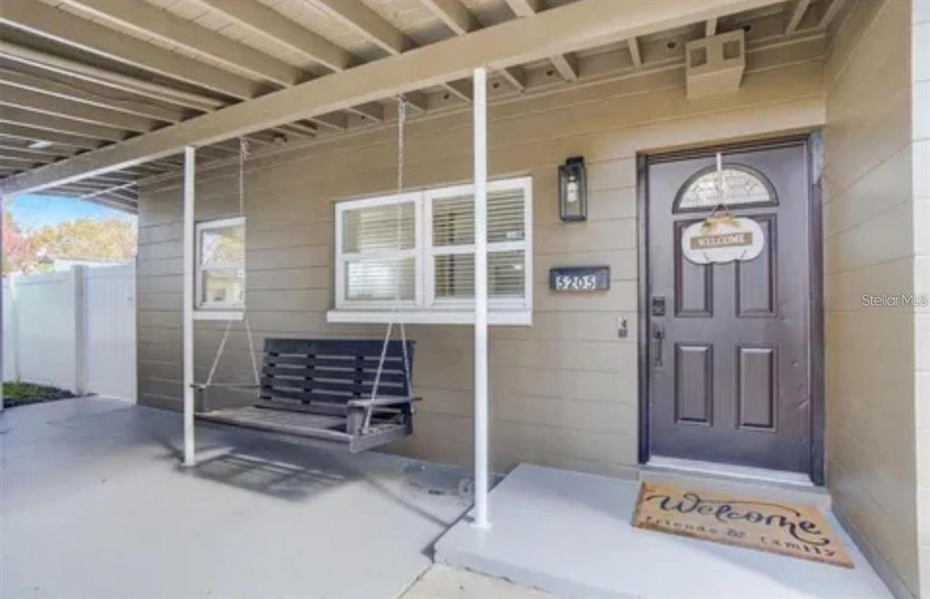 A covered front porch features a dark wooden swing, a front door, and a welcome mat — 5205 CHENAULT AVENUE, ORLANDO, FL