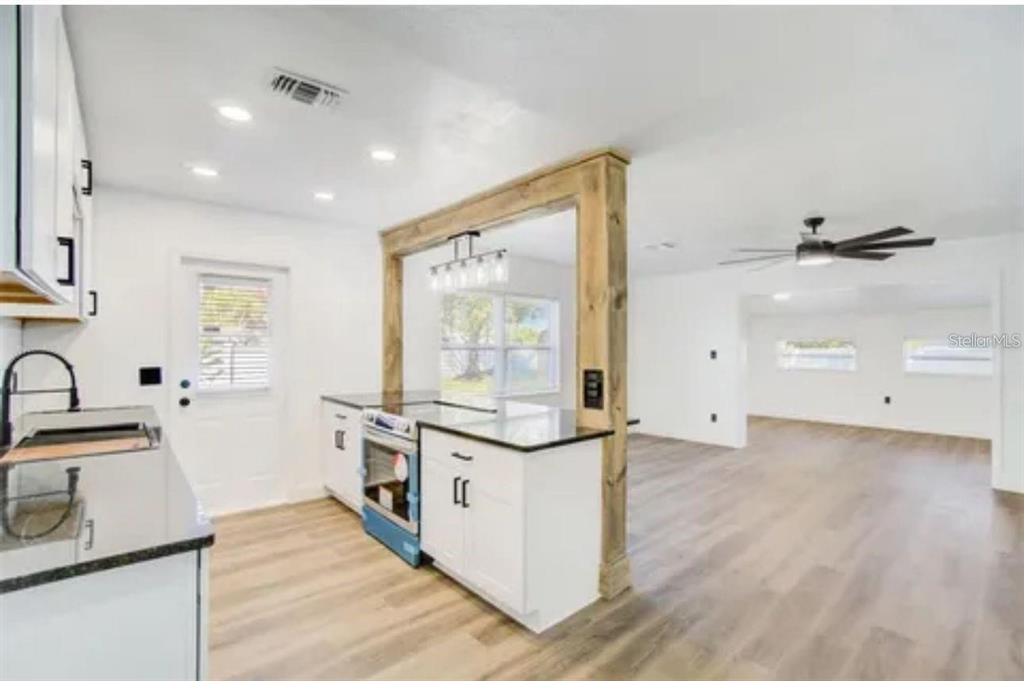 A kitchen with white cabinets and a wooden beam opening into a living area — 5205 CHENAULT AVENUE, ORLANDO, FL