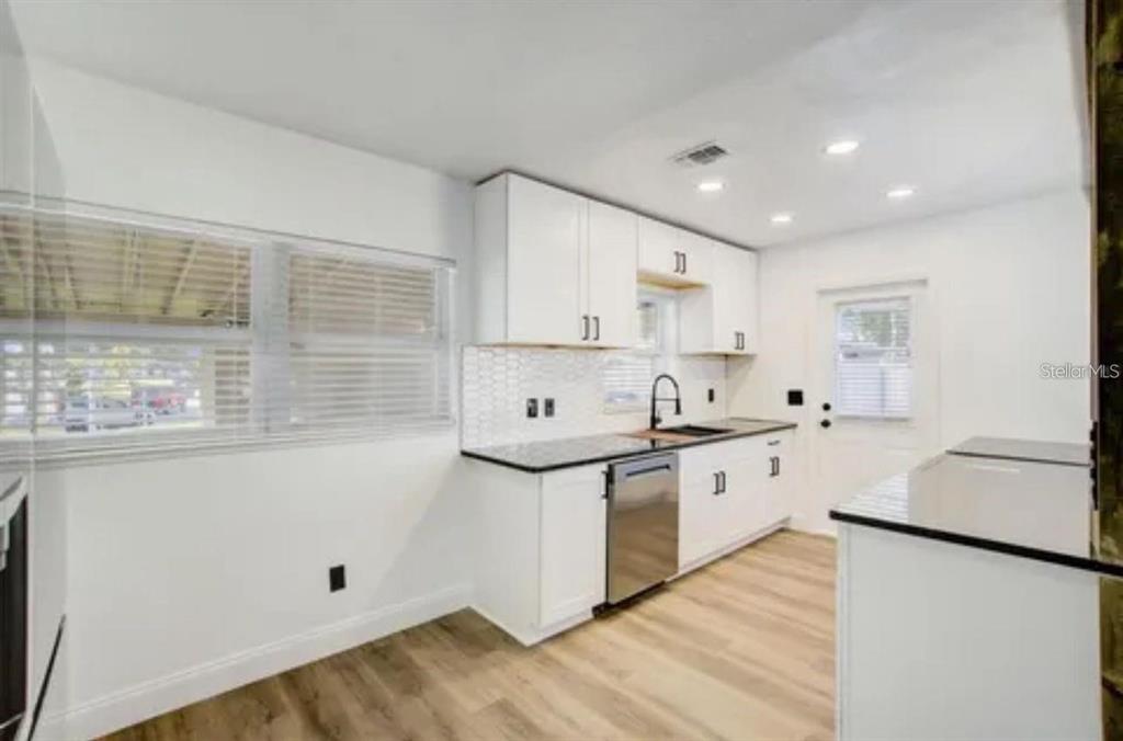 A kitchen with white cabinets, black countertops, stainless steel appliances, and light wood-look flooring — 5205 CHENAULT AVENUE, ORLANDO, FL