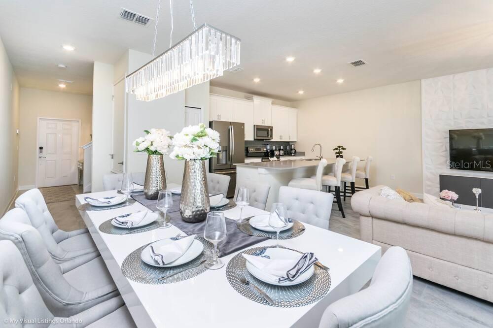 A dining area with a white table and chandelier opens into a modern kitchen — 1581 SANDBAGGER DRIVE, DAVENPORT, FL