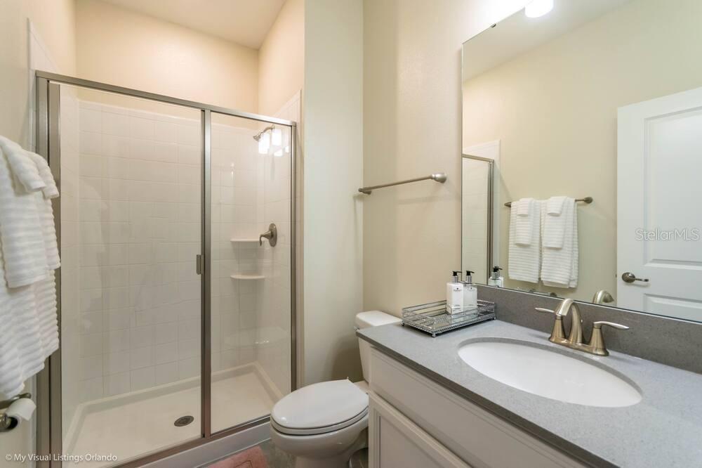 A bathroom features a glass-enclosed shower, a white vanity with a sink, and a toilet — 1581 SANDBAGGER DRIVE, DAVENPORT, FL