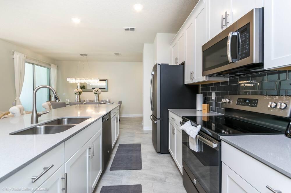 A modern kitchen features white cabinets, stainless steel appliances, and a large quartz island — 1581 SANDBAGGER DRIVE, DAVENPORT, FL