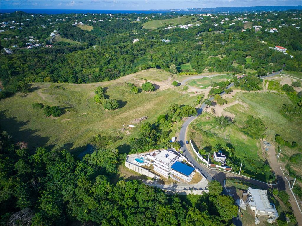An aerial view shows a modern house with a pool surrounded by lush green hills — Carr. 115 KM 11.4 INT SECTOR JULIO SOTO, RINCON, PR