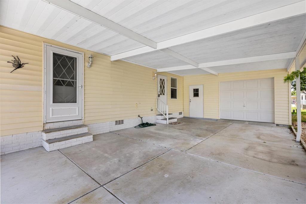 A concrete carport with a white garage door and two exterior doors on a house — 1616 BAYHILL DRIVE, LADY LAKE, FL