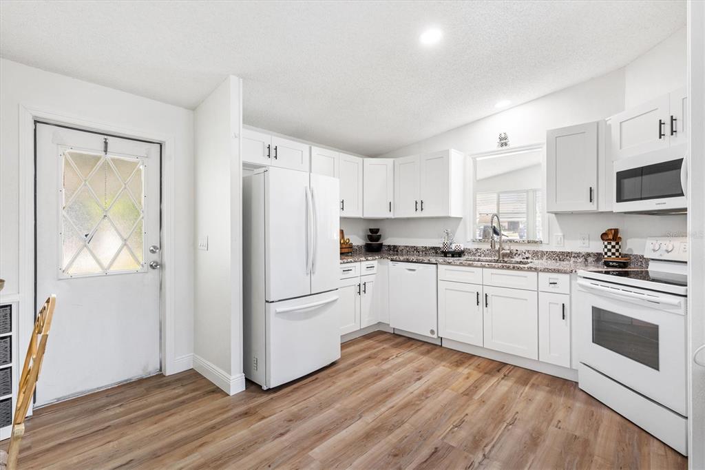 A kitchen features white cabinets, granite countertops, stainless steel appliances, and wood-look flooring — 1616 BAYHILL DRIVE, LADY LAKE, FL
