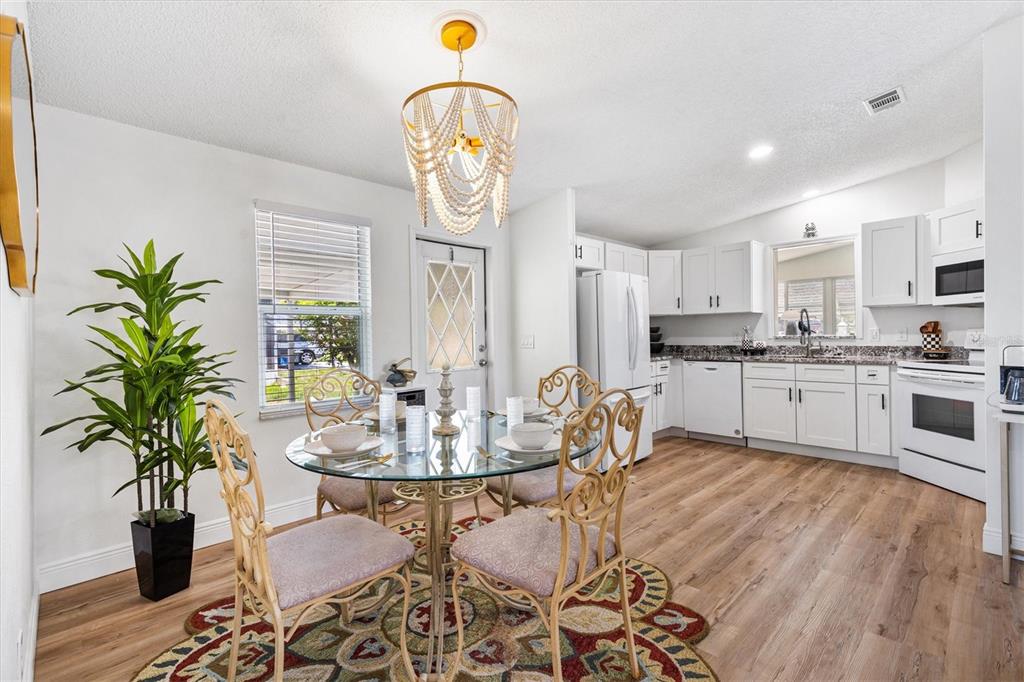 A dining area with a glass table and chandelier sits adjacent to a white kitchen — 1616 BAYHILL DRIVE, LADY LAKE, FL