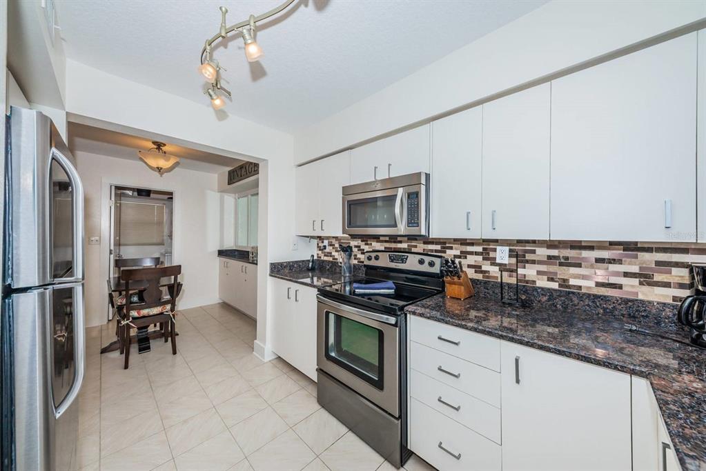 A kitchen with white cabinets, stainless steel appliances, dark granite countertops, and a tiled backsplash — 6083 BAHIA DEL MAR CIRCLE UNIT 460, ST PETERSBURG, FL