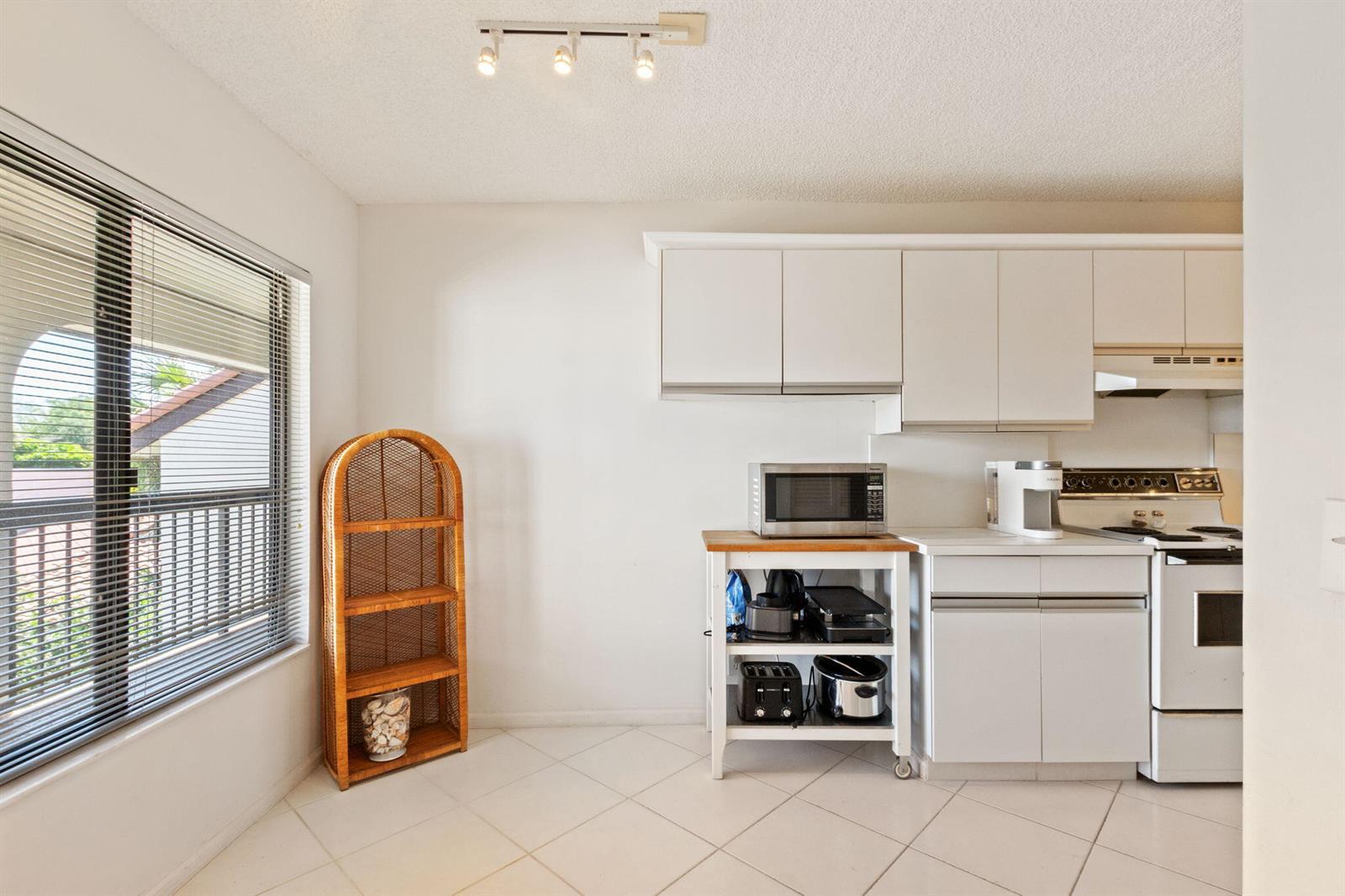 A kitchen features white cabinets, a rolling island, tile flooring, and a wicker shelf — 5380 Cedar Lake Drive # 303, Boynton Beach FL 33437, BOYNTON BEACH, FL