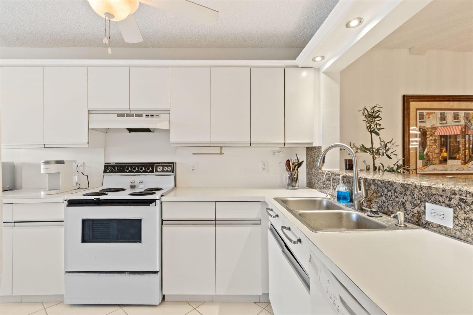 A kitchen features white cabinets, white appliances, a granite backsplash, and a double-basin sink — 5380 Cedar Lake Drive # 303, Boynton Beach FL 33437, BOYNTON BEACH, FL