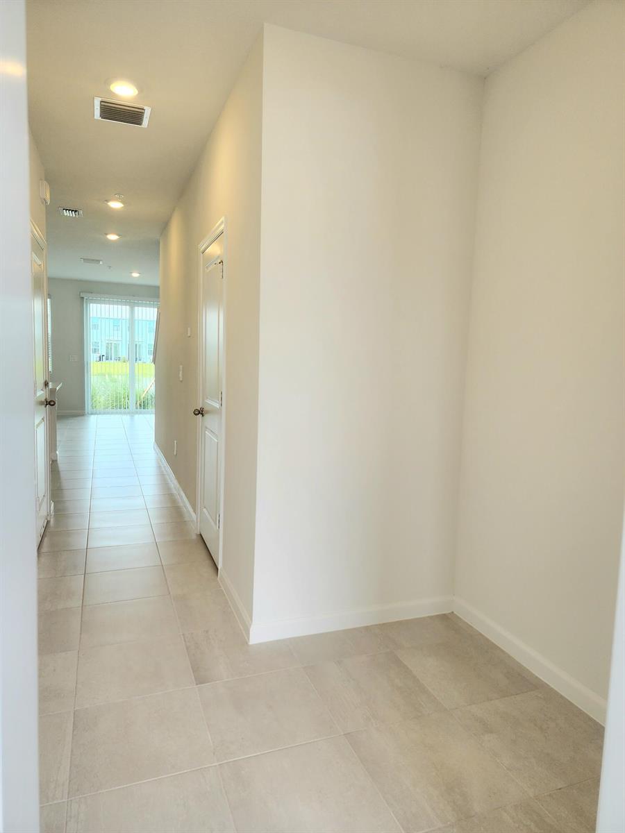 A hallway with light-colored tile flooring leads toward a glass sliding door at the end — 629 Salisbury Circle, Fort Pierce FL 34982, FORT PIERCE, FL