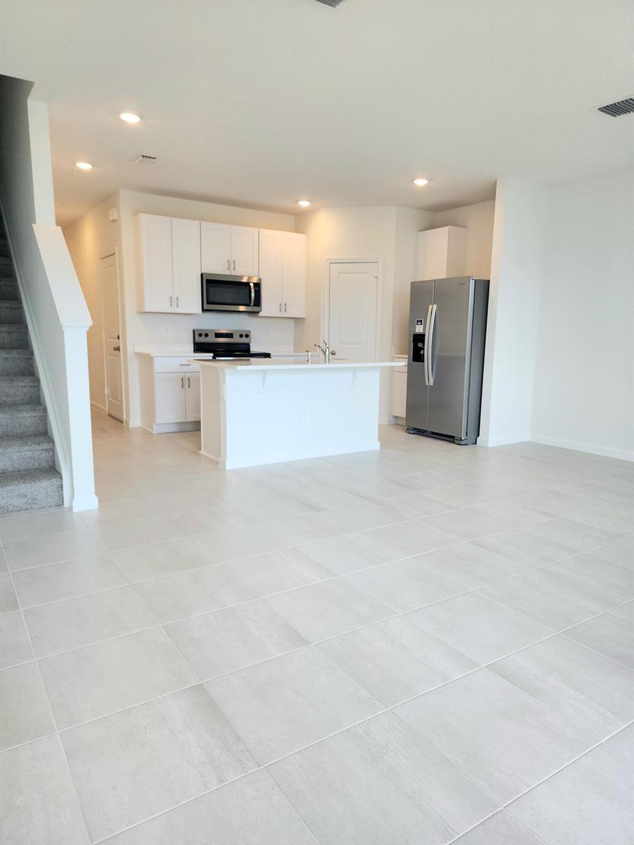 A modern kitchen features white cabinets, stainless steel appliances, a center island, and tile flooring — 629 Salisbury Circle, Fort Pierce FL 34982, FORT PIERCE, FL
