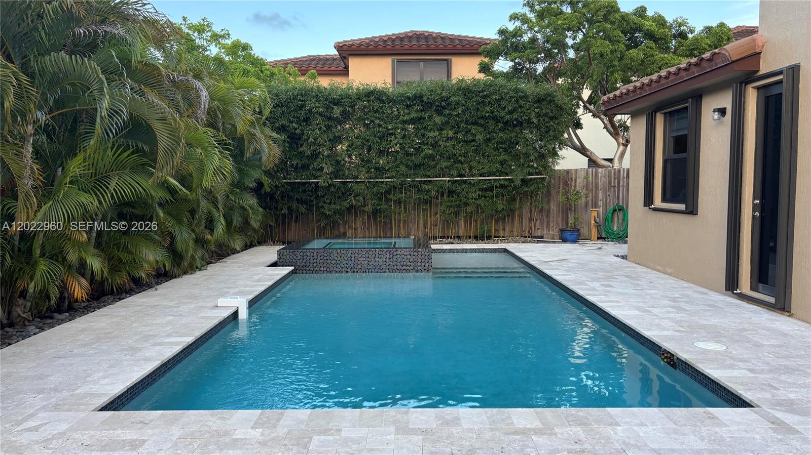 A rectangular swimming pool with an attached spa sits in a backyard with stone pavers — 157 NE 25th Ave, Homestead FL 33033, HOMESTEAD, FL