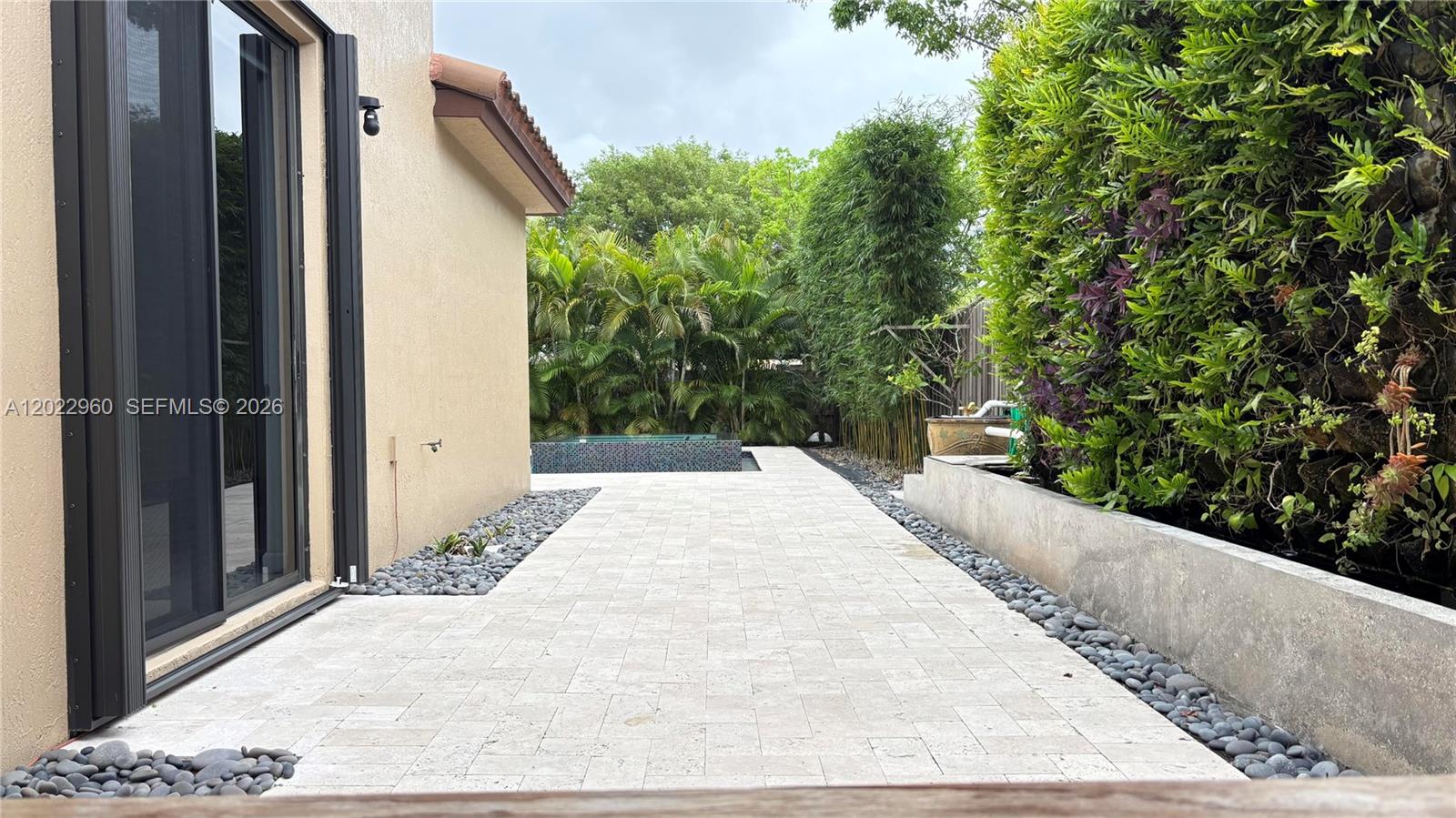 A paved patio leads toward a small pool surrounded by lush tropical landscaping — 157 NE 25th Ave, Homestead FL 33033, HOMESTEAD, FL