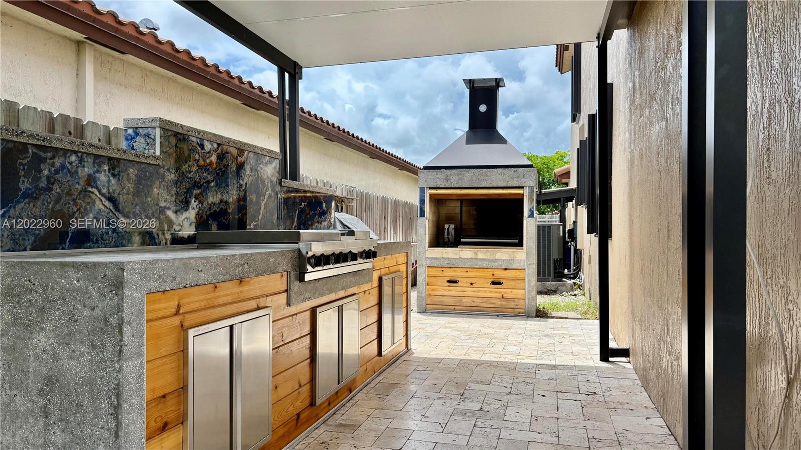An outdoor kitchen features a concrete countertop, wood cabinetry, and a separate stone fireplace — 157 NE 25th Ave, Homestead FL 33033, HOMESTEAD, FL