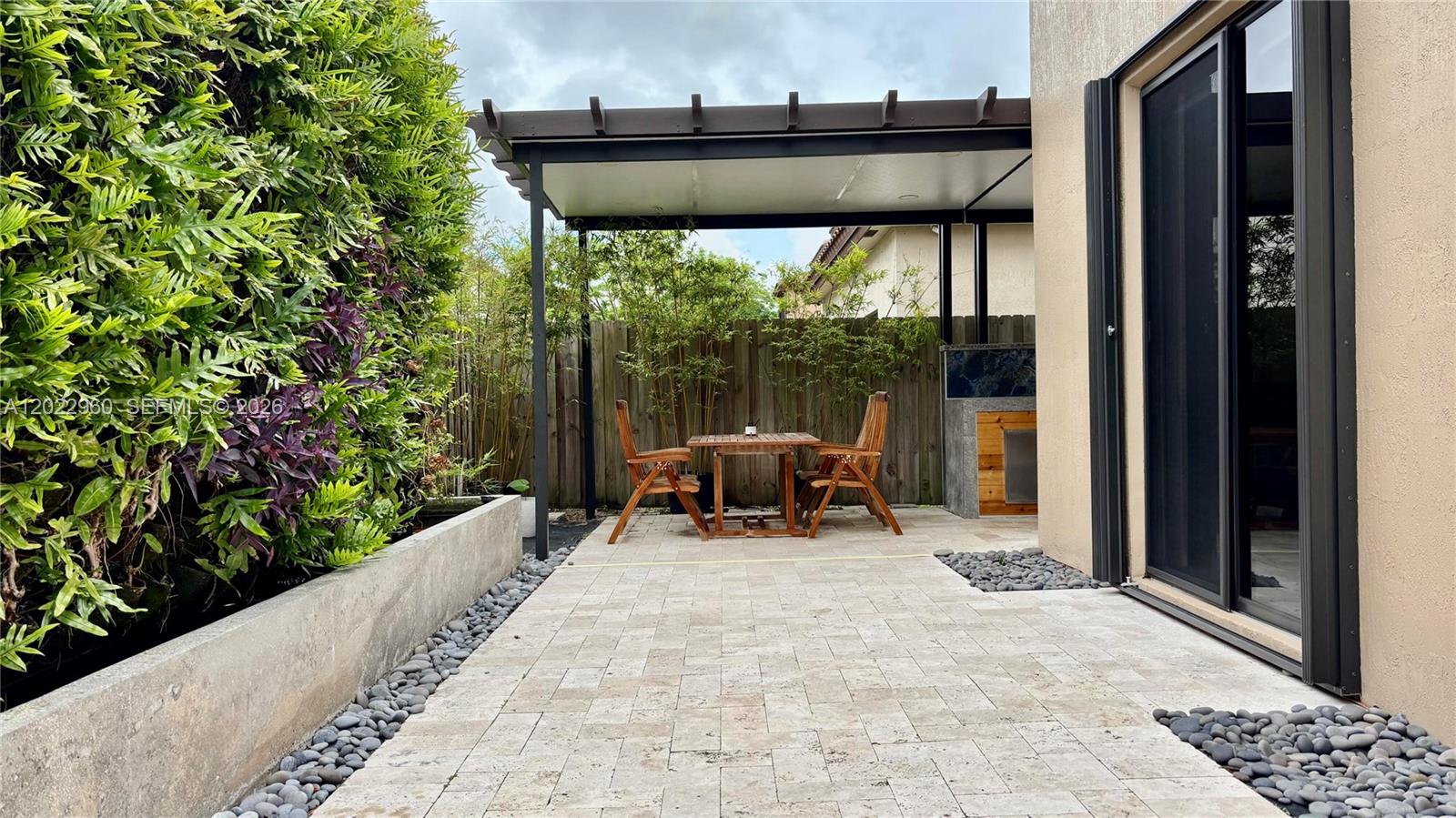 A paved patio features a covered dining area, a small outdoor kitchen, and lush landscaping — 157 NE 25th Ave, Homestead FL 33033, HOMESTEAD, FL