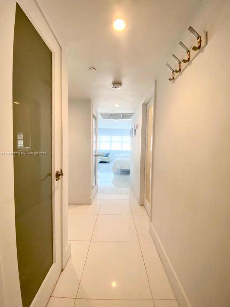 A bright hallway with white tile floors leads to a bedroom with large windows — 100 Lincoln Rd # 906, Miami Beach FL 33139, MIAMI BEACH, FL