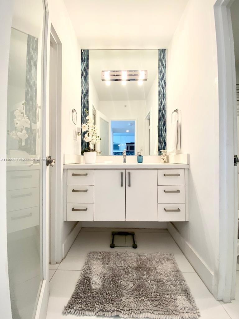 A bathroom features a white floating vanity, a large mirror, and blue mosaic tile accents — 100 Lincoln Rd # 906, Miami Beach FL 33139, MIAMI BEACH, FL
