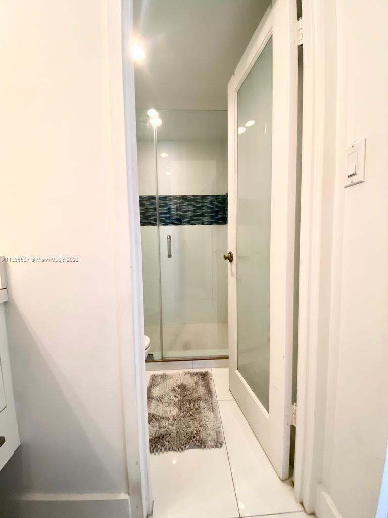 A bathroom features a glass-paneled door, a tiled shower, and a light-colored floor rug — 100 Lincoln Rd # 906, Miami Beach FL 33139, MIAMI BEACH, FL