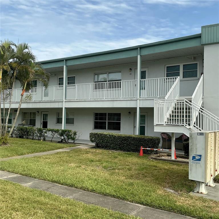A two-story apartment building features a white exterior, a metal staircase, and a palm tree — 5267 81ST ST N UNIT 26, ST PETERSBURG, FL