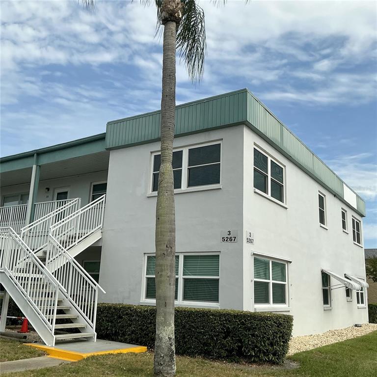 A two-story apartment building exterior features white stucco walls, green trim, and an outdoor staircase — 5267 81ST ST N UNIT 26, ST PETERSBURG, FL