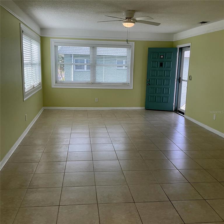 An empty room with light green walls, tiled flooring, a ceiling fan, and an entry door — 5267 81ST ST N UNIT 26, ST PETERSBURG, FL